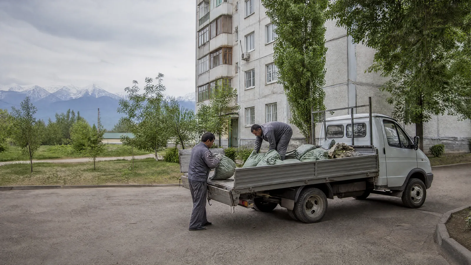 Бортовая газель TRASHOFF с открытым кузовом, грузчики укладывают стройотходы во дворе алматинской новостройки