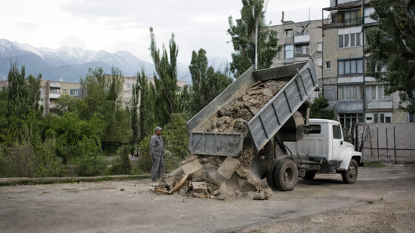 ЗИЛ-самосвал во дворе Алматы, кузов поднят, из него высыпается строительный мусор