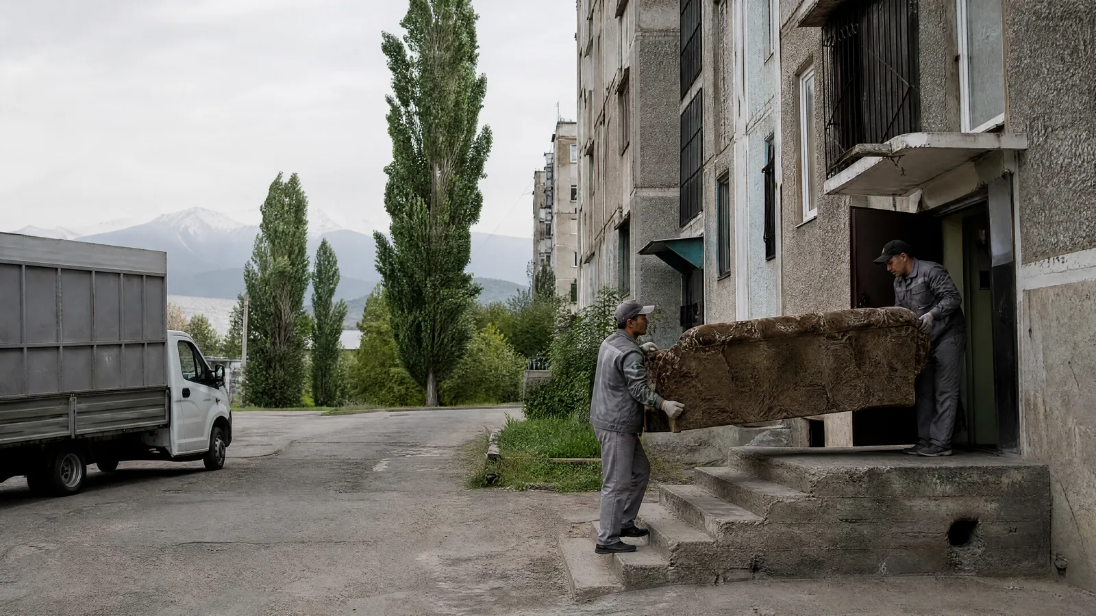 Loaders carrying an old sofa out of an apartment building entrance in Almaty