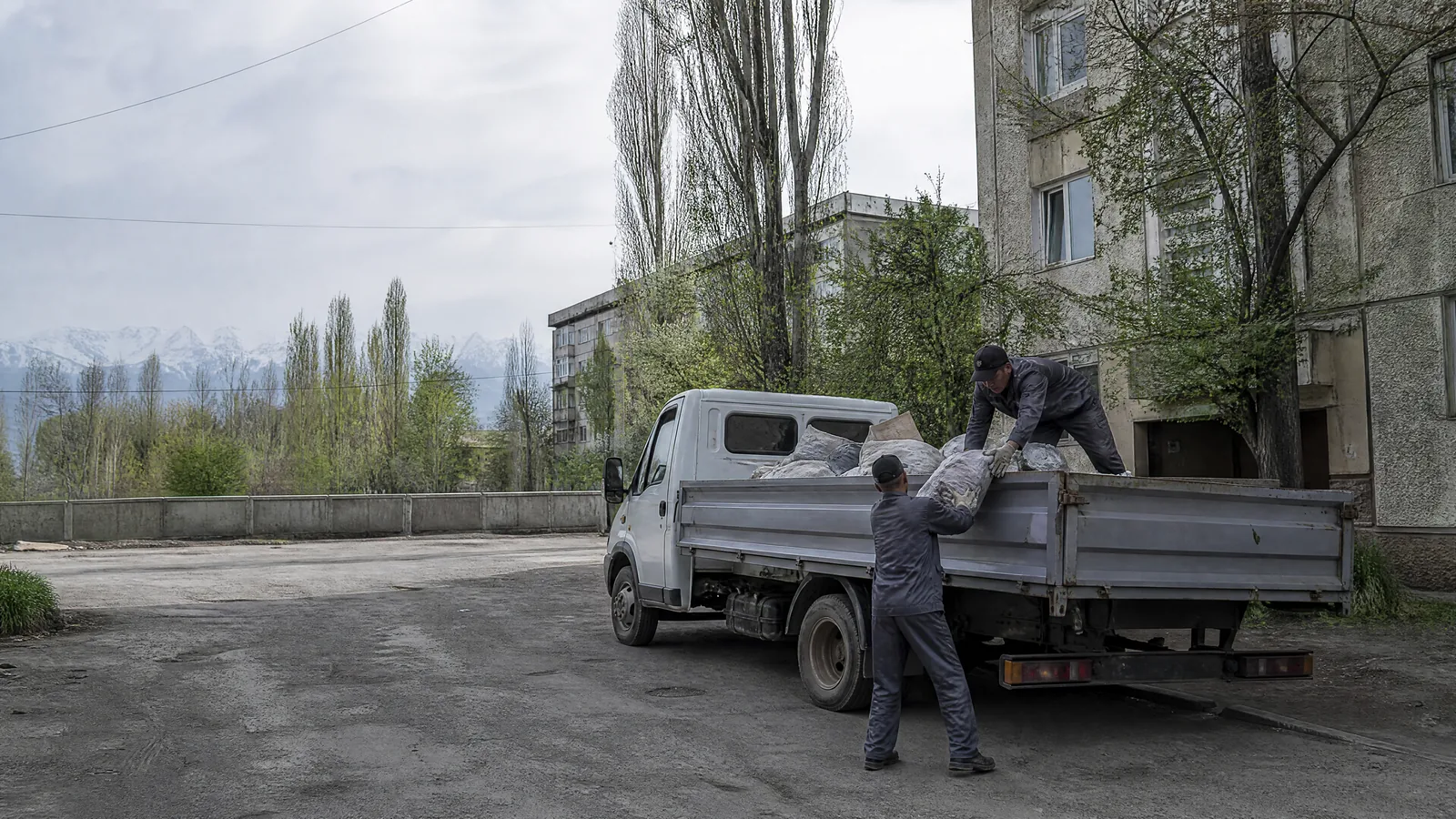 Грузчики TRASHOFF загружают мешки с твёрдыми бытовыми отходами в кузов газели во дворе алматинской многоэтажки