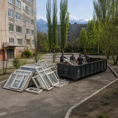 Old windows and double-glazed units stored in a residential complex courtyard before removal